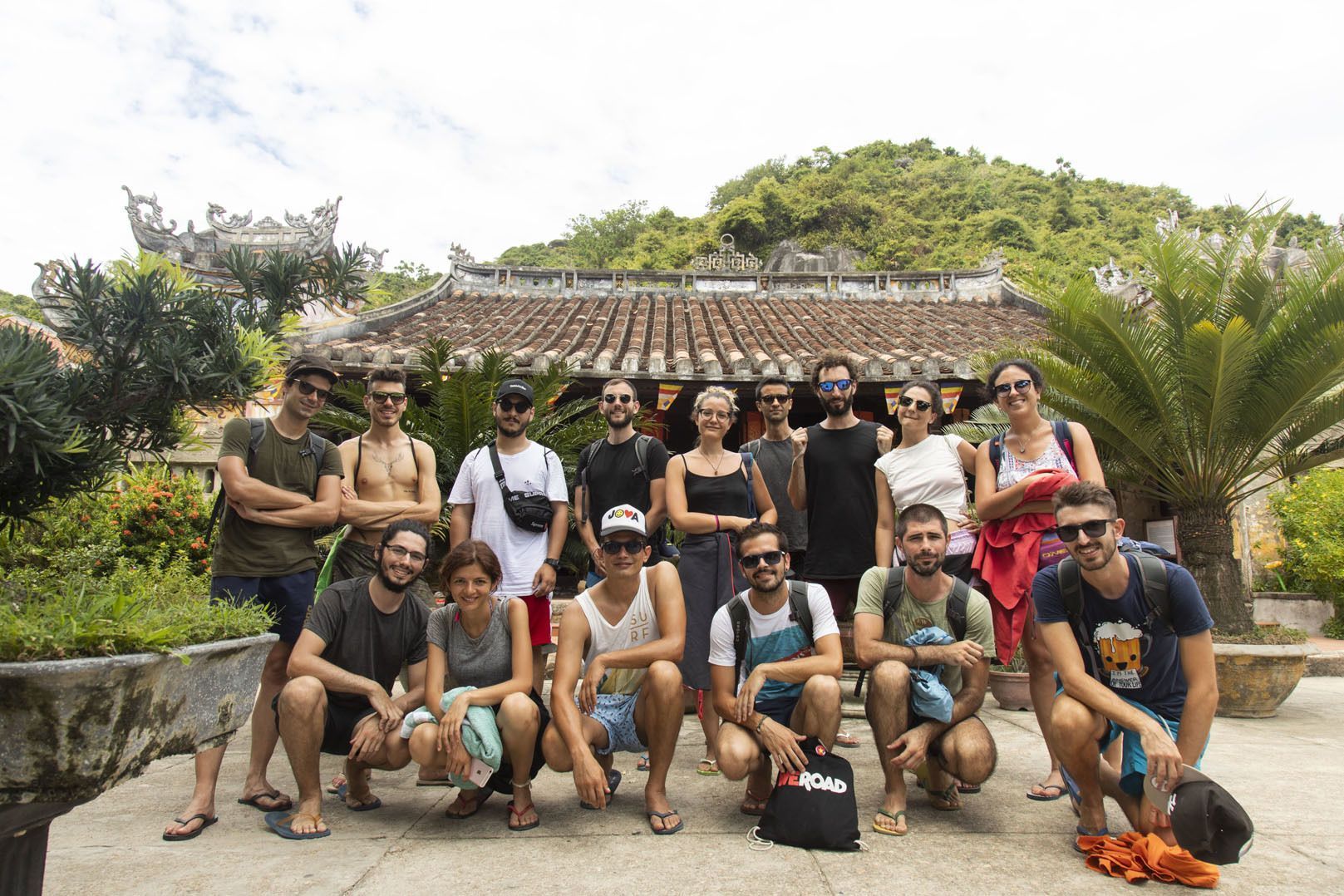 Un grupo de WeRoad posa para una foto frente a un edificio tradicional con techo de tejas, rodeado de exuberante vegetación.