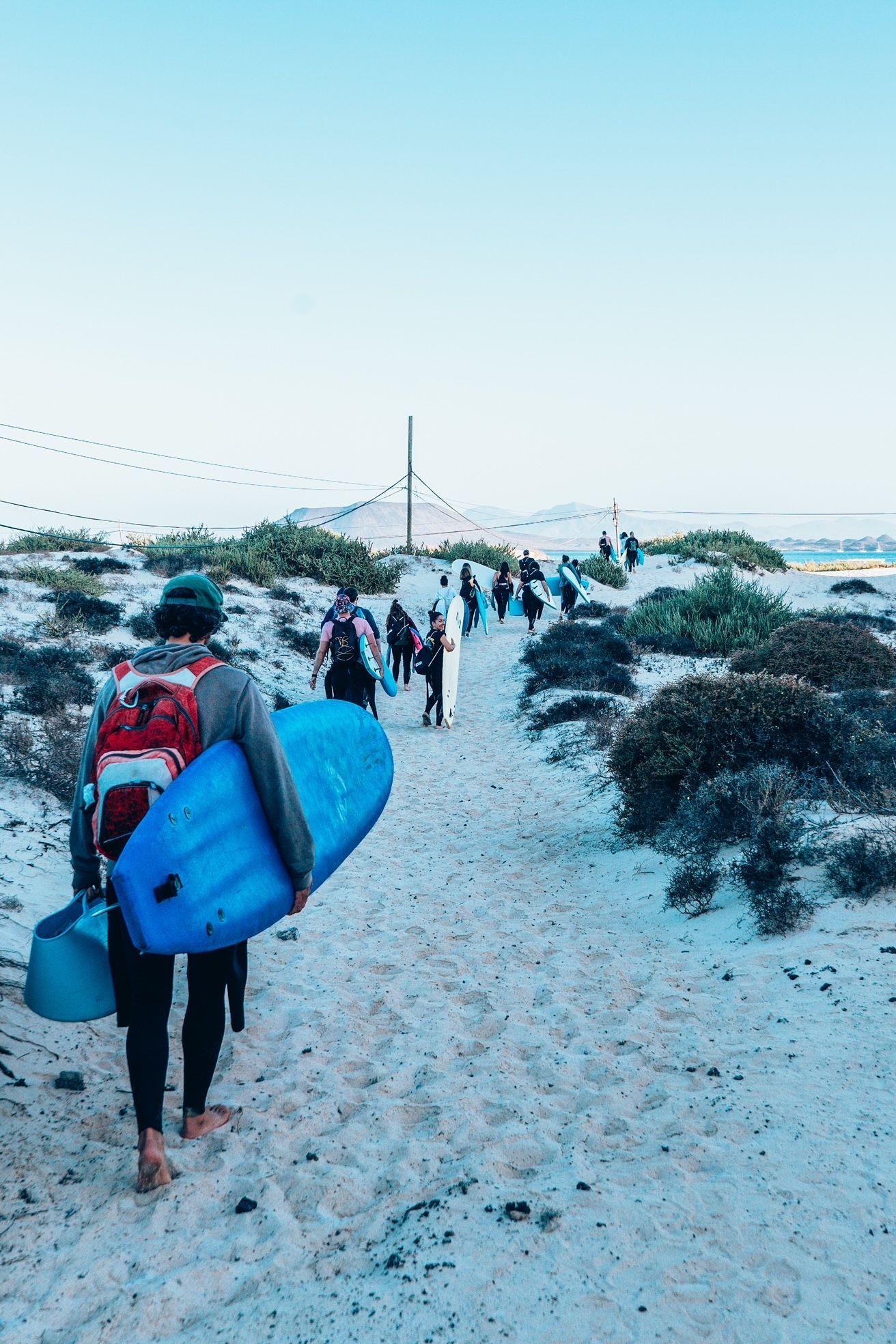 Un viaggio di gruppo WeRoad con tavole da surf e bodyboard che percorre un sentiero sabbioso verso il mare.