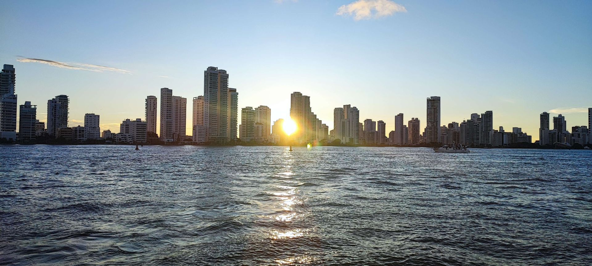 Eine Skyline hoher Gebäude, vom Wasser aus bei Sonnenuntergang gesehen, mit der Spiegelung der Sonne auf den Wellen.