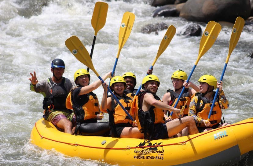 Un gruppo WeRoad sorride e alza le pagaie gialle mentre fa rafting su un gommone.