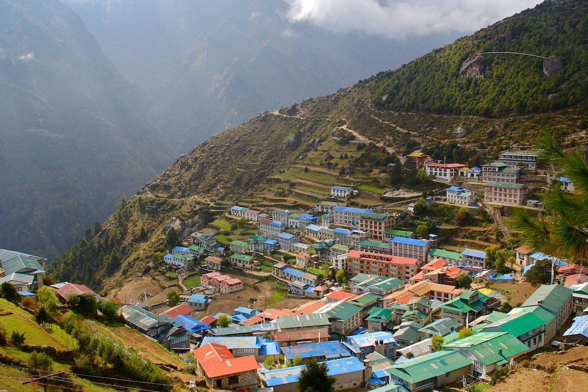 Una vista dall'alto di un villaggio con tetti colorati blu, verdi e rossi, costruito sui pendii terrazzati di una montagna ripida.