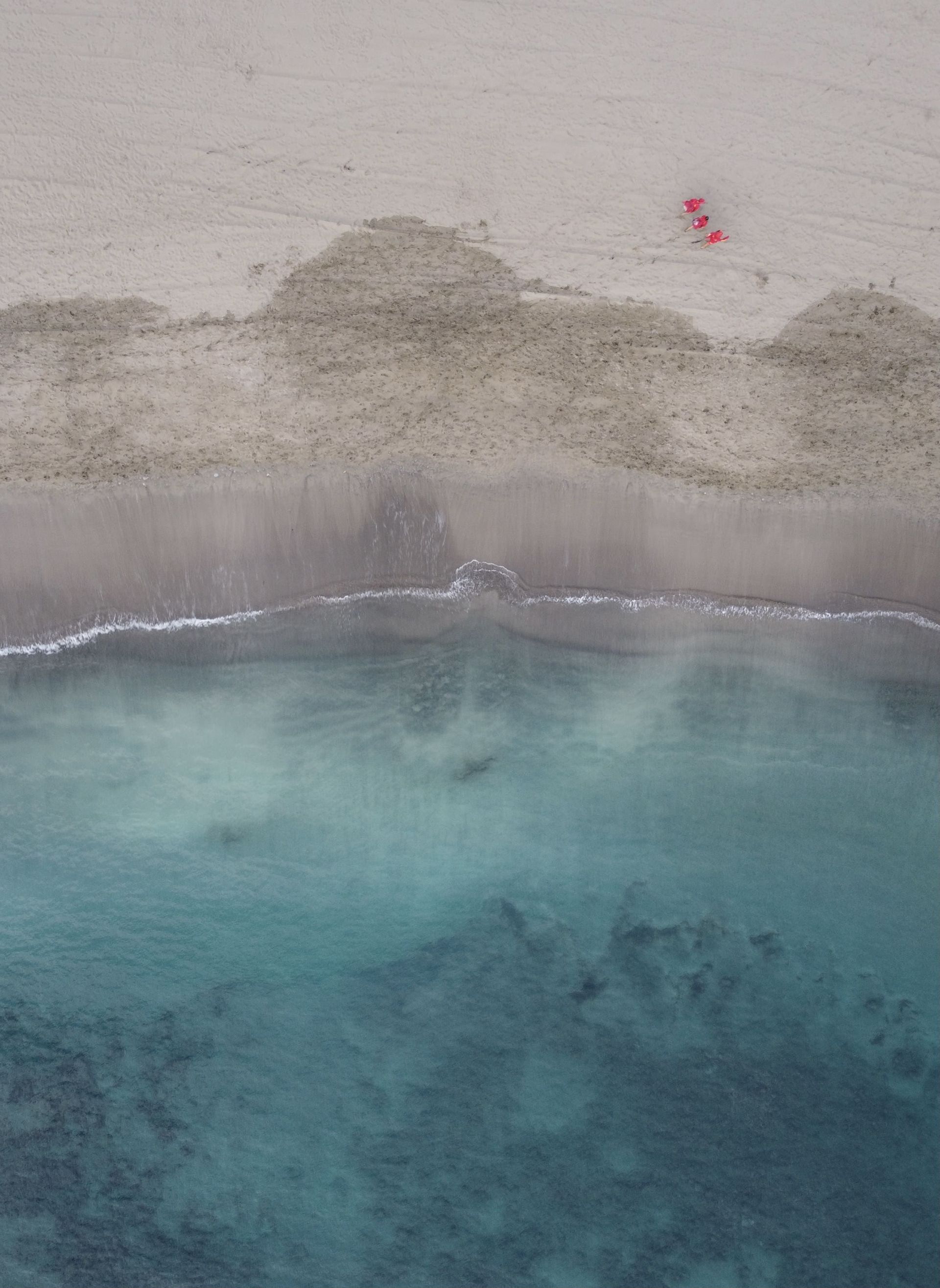 Una vista aérea de tres kayaks rojos descansando en una playa de arena junto a aguas turquesas claras.