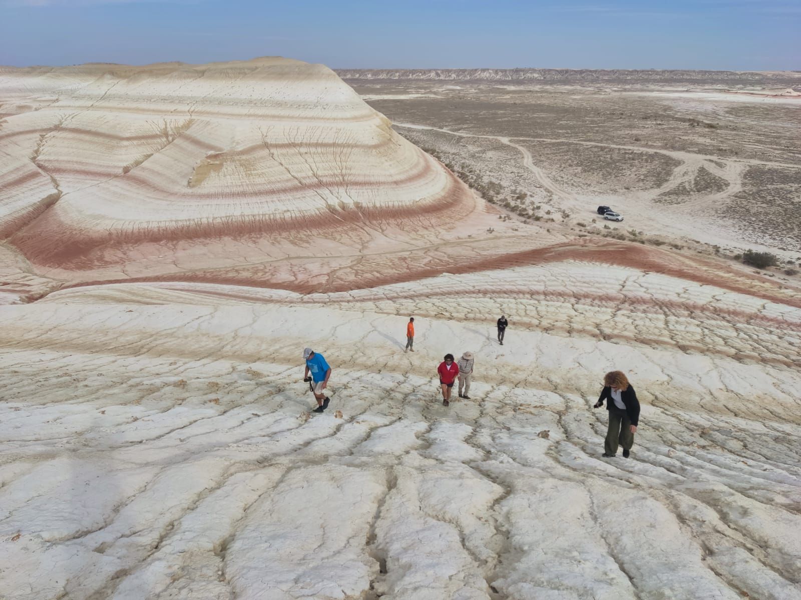 Un grupo de WeRoad camina sobre tierra blanca agrietada frente a grandes colinas rayadas y coloridas bajo un cielo amplio.