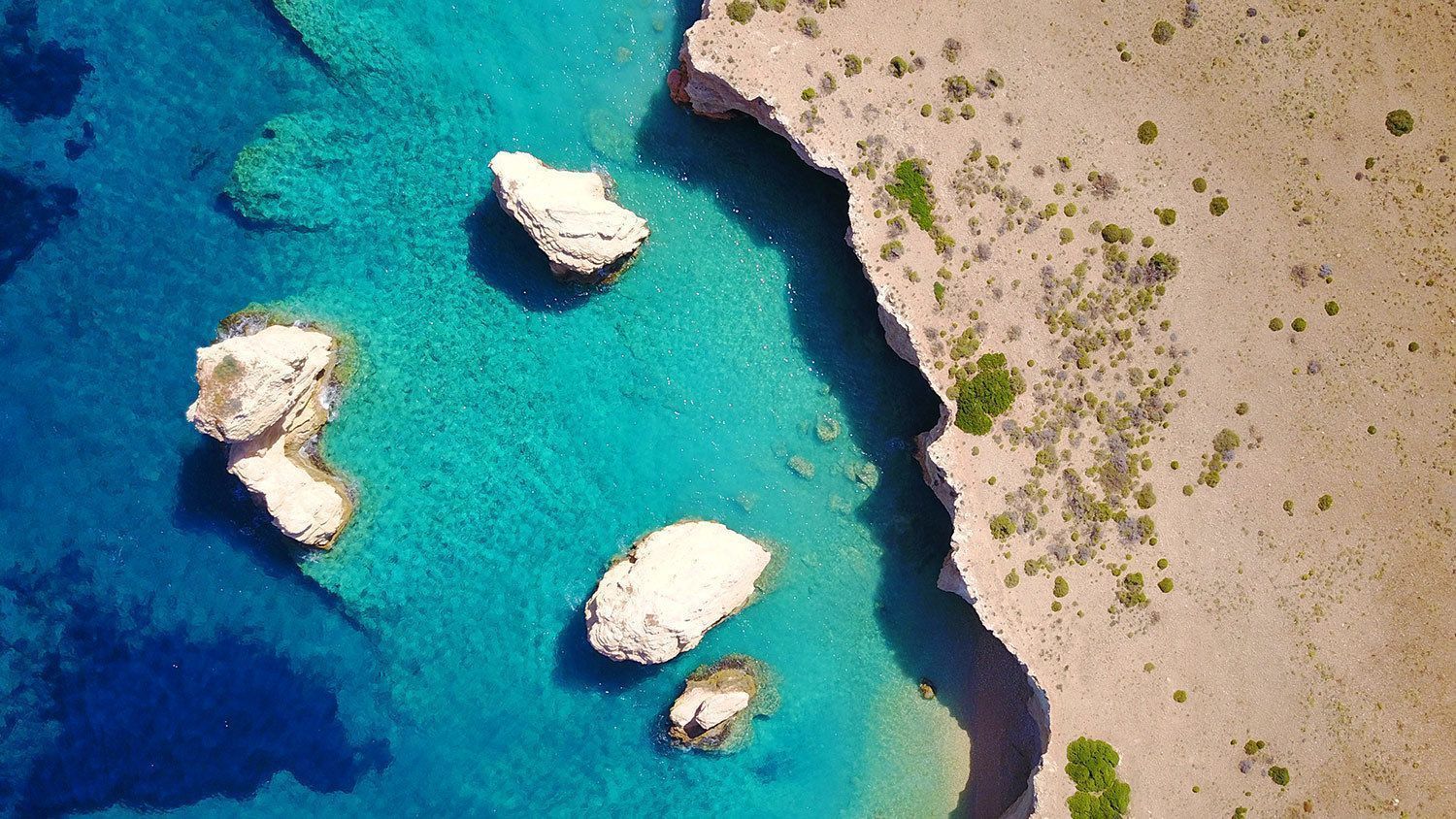 Vista aerea di formazioni rocciose bianche sparse nell'acqua turchese dell'oceano accanto a una falesia costiera sabbiosa