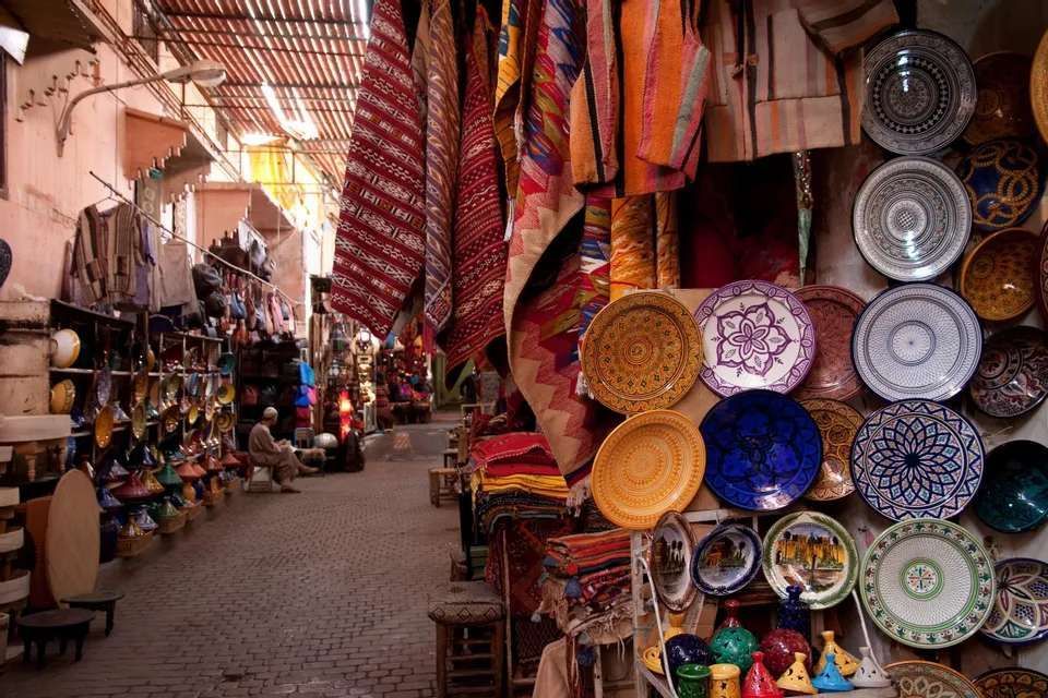 A view down a narrow cobblestone market alley lined with shops selling colorful ceramic plates and traditional textiles.