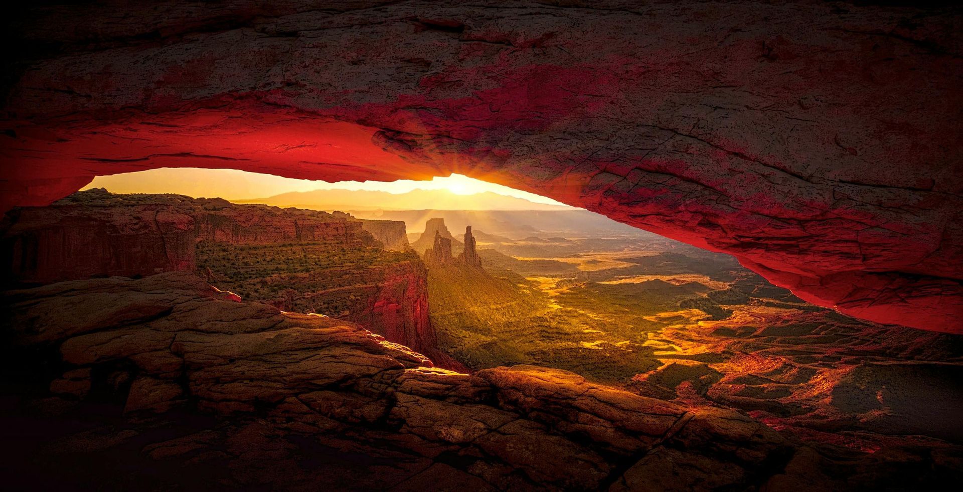 Il sole sorge su un vasto paesaggio di canyon, con la vista incorniciata dall'apertura di un enorme arco di roccia rossa.