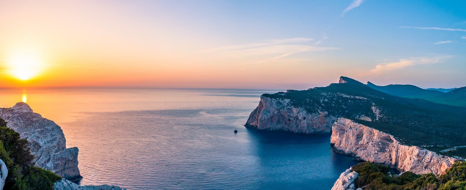 Il sole cala all'orizzonte sull'oceano, tingendo di luce dorata le scogliere frastagliate lungo la costa.