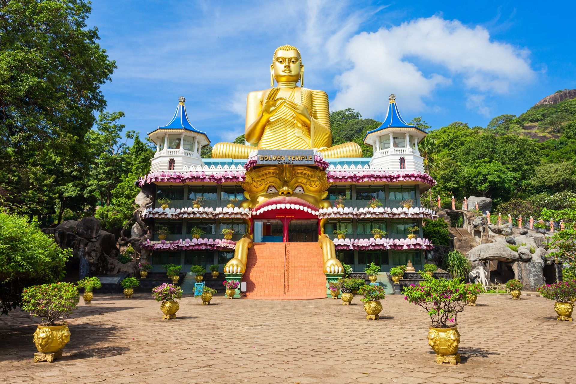 Una gigantesca statua dorata di Buddha si erge in cima all'ornato edificio del Tempio d'Oro, con scale che conducono a un grande ingresso a bocca di mostro.