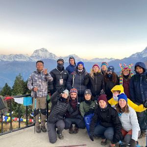 Un viaje en grupo de WeRoad posa para una foto en un mirador de montaña, con picos nevados al fondo durante el amanecer.