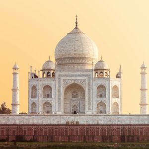 Un grande mausoleo simmetrico in marmo bianco con una cupola centrale e quattro minareti si staglia contro un cielo dorato al tramonto.