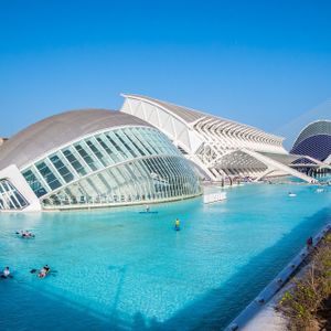 Moderni edifici architettonici bianchi vicino a una piscina di acqua turchese, con persone che praticano kayak e paddleboard sotto un cielo sereno.