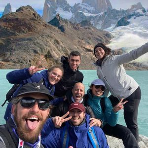 Un grupo de WeRoad se toma una selfie sonriente junto a un lago turquesa con montañas nevadas de fondo.