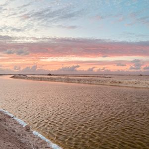 Salt pans with channels of water reflecting a colorful sunset sky with pink and blue clouds.