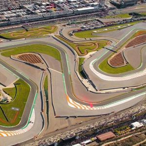 Vista aerea di un ampio e sinuoso circuito automobilistico con curve multiple, tribune e aree verdi interne.
