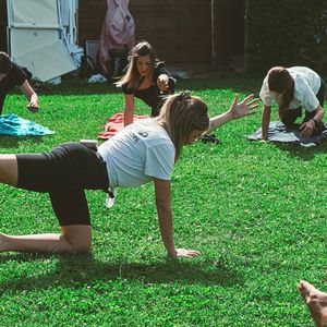 Un viaggio di gruppo WeRoad mentre pratica una posa yoga di equilibrio su un prato verde brillante.