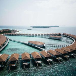 An aerial view of a resort with overwater bungalows arranged in a curve above the turquoise ocean.