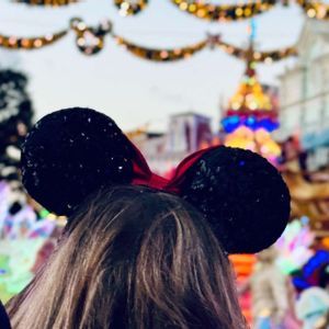 Der Hinterkopf einer Person mit schwarzen Pailletten-Mausohren, vor dem Hintergrund einer unscharfen, festlichen Parade.