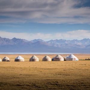 Une rangée de yourtes dans une plaine herbeuse, face à un lac et une chaîne de montagnes lointaine.