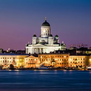 La Cattedrale illuminata di Helsinki e i palazzi sul lungomare della città, visti dall'acqua al crepuscolo.