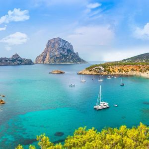 Una vista dall'alto di una cala con una spiaggia sabbiosa, dove le persone nuotano nelle acque limpide e turchesi sotto un cielo azzurro brillante.
