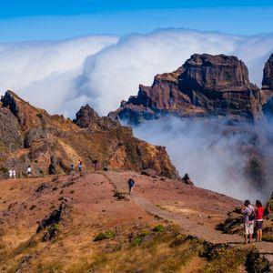 Una persona di un viaggio di gruppo WeRoad, con muta e casco, si tuffa in una piscina naturale vicino a una cascata mentre altri guardano.