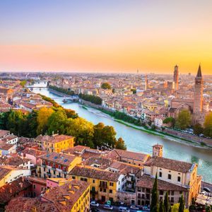 Vista aerea di una città storica con tetti rossi e un fiume sinuoso sotto un cielo dorato al tramonto.