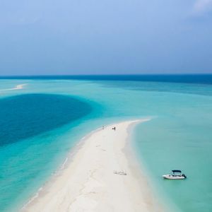 Una vista aerea di un lungo banco di sabbia bianca che si curva in acque oceaniche turchesi dove è ancorata una piccola barca.