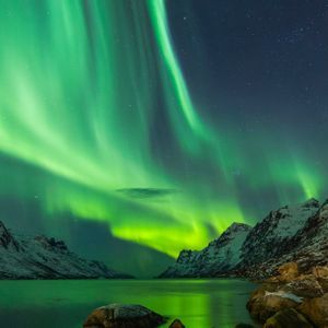 Helle grüne Bänder des Nordlichts leuchten am sternenklaren Nachthimmel über einer verschneiten Bergkette.