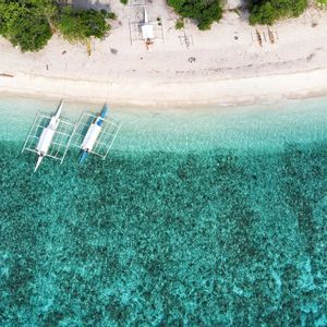 Una vista aerea di barche a bilanciere ormeggiate su una spiaggia di sabbia bianca che costeggia acque turchesi e limpide con una barriera corallina visibile.