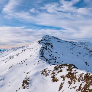 Una cima montuosa innevata con una cresta rocciosa sotto un cielo blu con nuvole sparse.