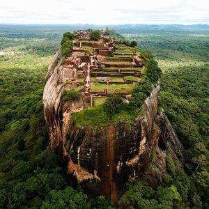 Vista aerea di rovine antiche e giardini costruiti sulla cima di un grande monolite roccioso circondato da una fitta foresta verde