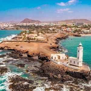 Vista aerea di un faro bianco su una penisola rocciosa vicino a una città costiera con acqua turchese
