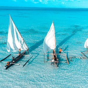 Vista aérea de un viaje en grupo de WeRoad navegando en tres canoas tradicionales a través de aguas turquesas poco profundas.
