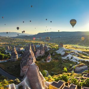 Decenas de globos aerostáticos flotan sobre un valle con formaciones rocosas únicas y un pueblo al amanecer.