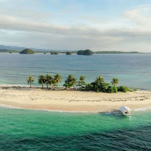 Una veduta aerea di un viaggio di gruppo WeRoad su una piccola isola tropicale, con sabbia bianca, palme e una barca ormeggiata in acqua turchese.