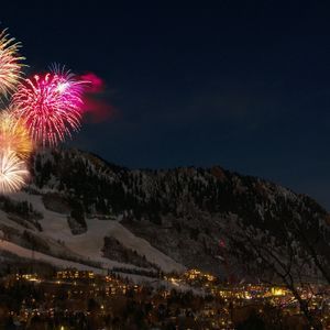 Fuochi d'artificio colorati esplodono su un villaggio montano innevato di notte.