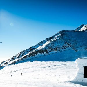 Uno sciatore in salto a mezz'aria su una montagna innevata sotto un cielo azzurro.