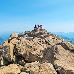 Un voyage de groupe WeRoad se tient sur un sommet rocheux, surplombant une vaste chaîne de montagnes sous un ciel bleu clair.