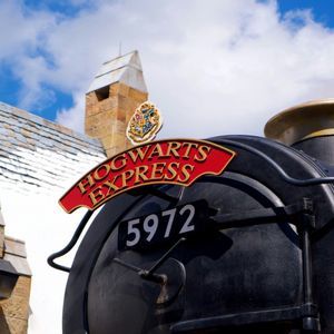 Primo piano dal basso del treno a vapore Hogwarts Express, numero 5972, con un edificio in pietra sullo sfondo.