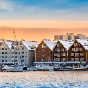 Un panorama d'un port enneigé avec des bateaux amarrés le long d'un quai bordé de bâtiments traditionnels au coucher du soleil.