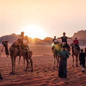 Un viaje en grupo de WeRoad posando para una foto en camellos en un desierto con montañas rocosas durante el atardecer.