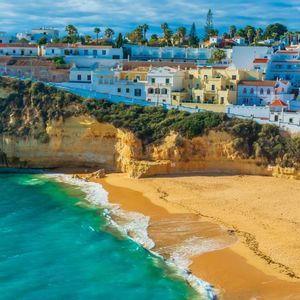 A coastal town with white buildings perched on cliffs above a golden sand beach and a turquoise ocean.