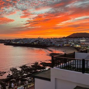 Città costiera con edifici bianchi, vista da un balcone sotto un cielo spettacolare arancione e rosso al tramonto.