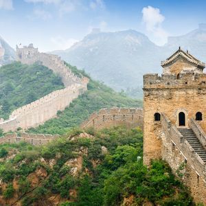 Una larga muralla de piedra con torres de vigilancia serpentea por las cimas de exuberantes montañas verdes bajo un cielo brumoso.