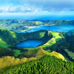 Vue aérienne de plusieurs lacs de cratère bleus nichés dans des collines volcaniques verdoyantes, avec l'océan en arrière-plan.