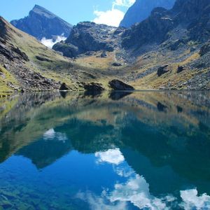 Un lago di montagna calmo e limpido riflette perfettamente le cime rocciose e il cielo blu, con un gruppo WeRoad che fa escursioni su un sentiero lungo il lago.