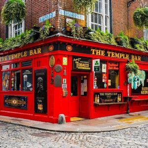La fachada roja brillante del pub The Temple Bar en una esquina de calle adoquinada, decorada con plantas colgantes.