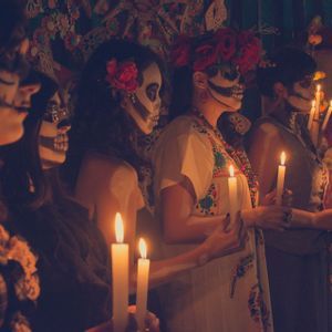 Un viaggio di gruppo WeRoad di donne con make-up da teschio che tengono candele accese davanti a un altare del Giorno dei Morti.
