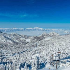 Ein Panoramablick vom Sessellift zeigt eine weite Landschaft aus schneebedeckten Bergen und Wäldern unter strahlend blauem Himmel.