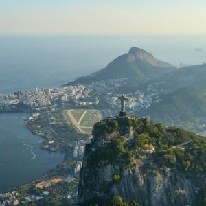 An aerial view of the Christ the Redeemer statue on Corcovado mountain, overlooking the city of Rio de Janeiro, a lake, and the ocean.